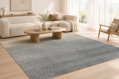 An abstract rectangular rug or textile with a textured, speckled finish, featuring a color gradient that transitions from a warm cream/beige at the top to a medium grey at the bottom.