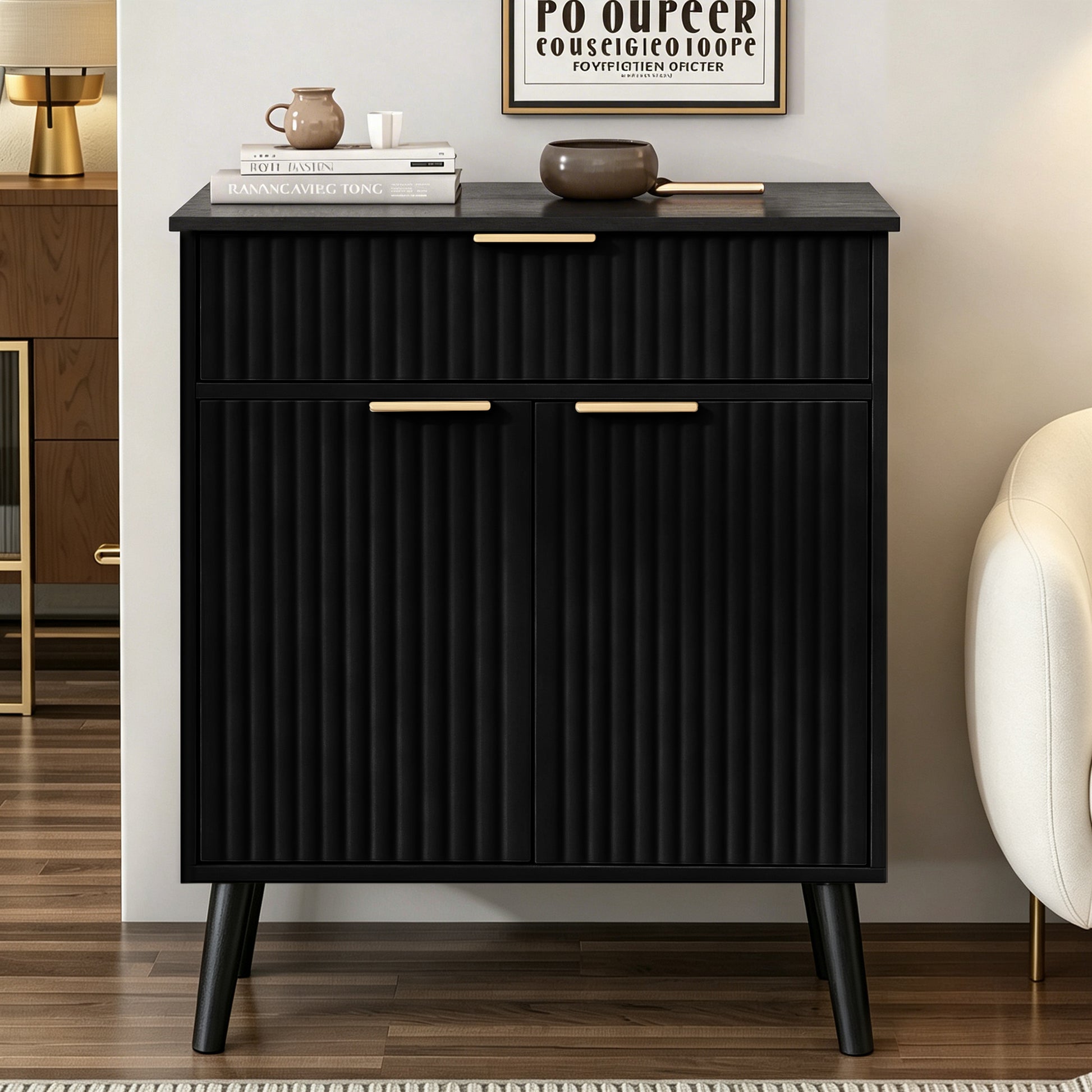 A modern black cabinet with vertical fluting, tapered legs, and gold-tone handles, styled in a living room setting next to a armchair.