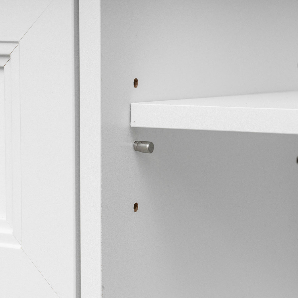 Close-up detail of a white shelf mounted on a white cabinet wall, showing a silver metal shelf pin and pre-drilled mounting holes.
