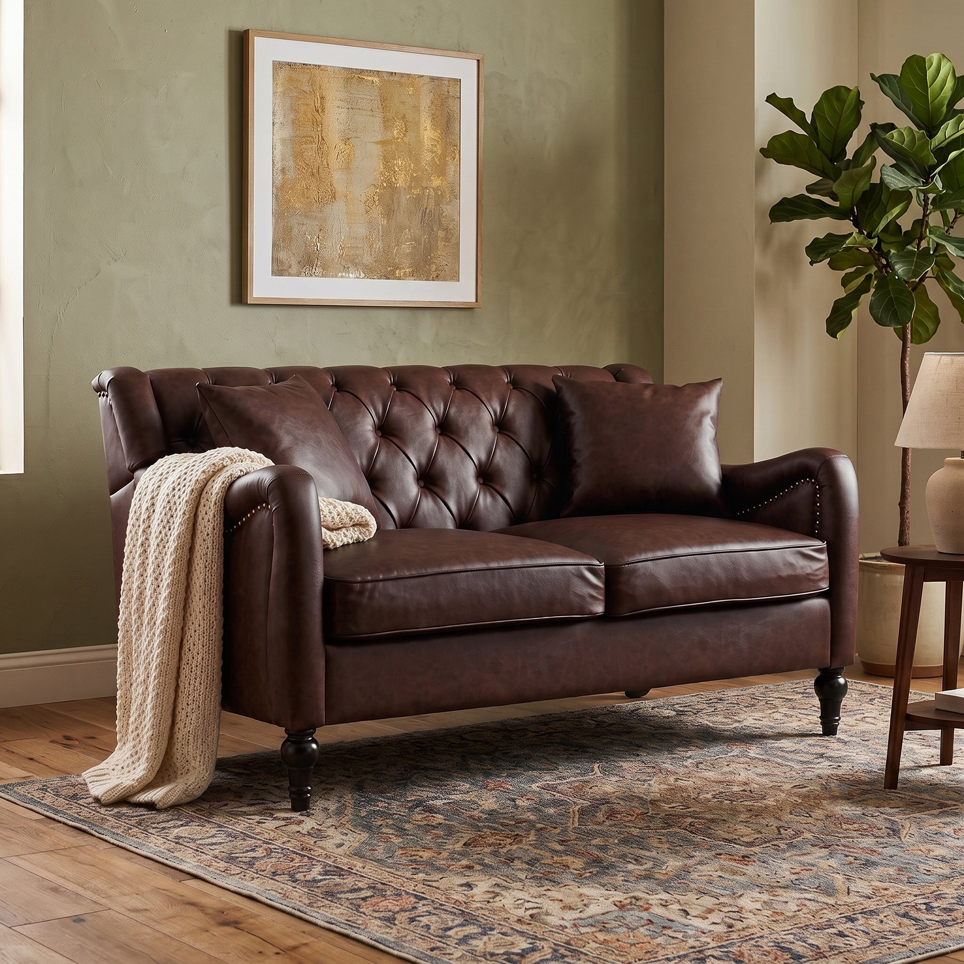 A Dark Brown Loveseat leather loveseat with tufted button detailing on the backrest and seat, styled in a living room setting with a cream knit throw blanket, a patterned area rug, a wooden side table, and a potted fiddle-leaf fig plant.