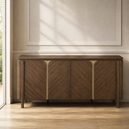 A mid-century modern wooden sideboard with chevron grain patterns and brass-finished vertical dividers, positioned against a beige wall with decorative molding and soft window shadows.