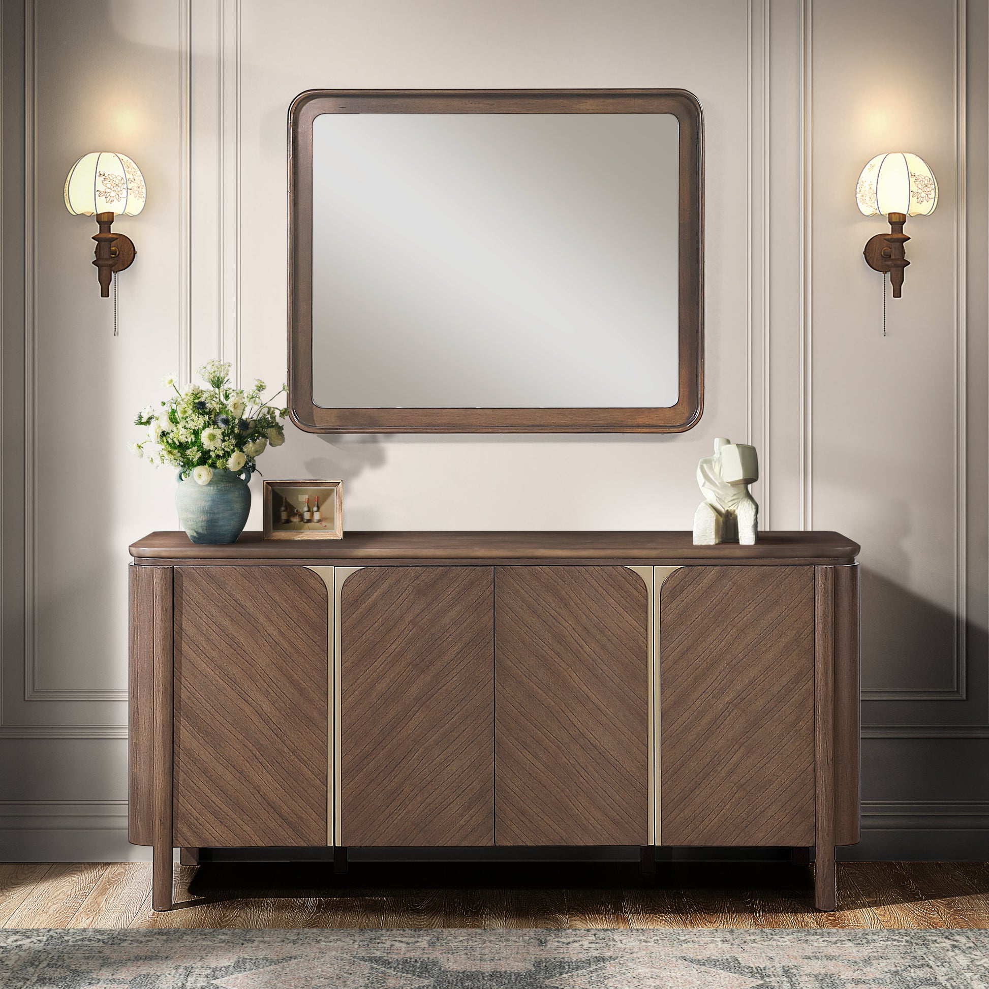 A mid-century modern wooden credenza or sideboard with a matching rectangular wall mirror, styled in a classic room setting with two wall sconces, a vase of flowers, and a small decorative sculpture.