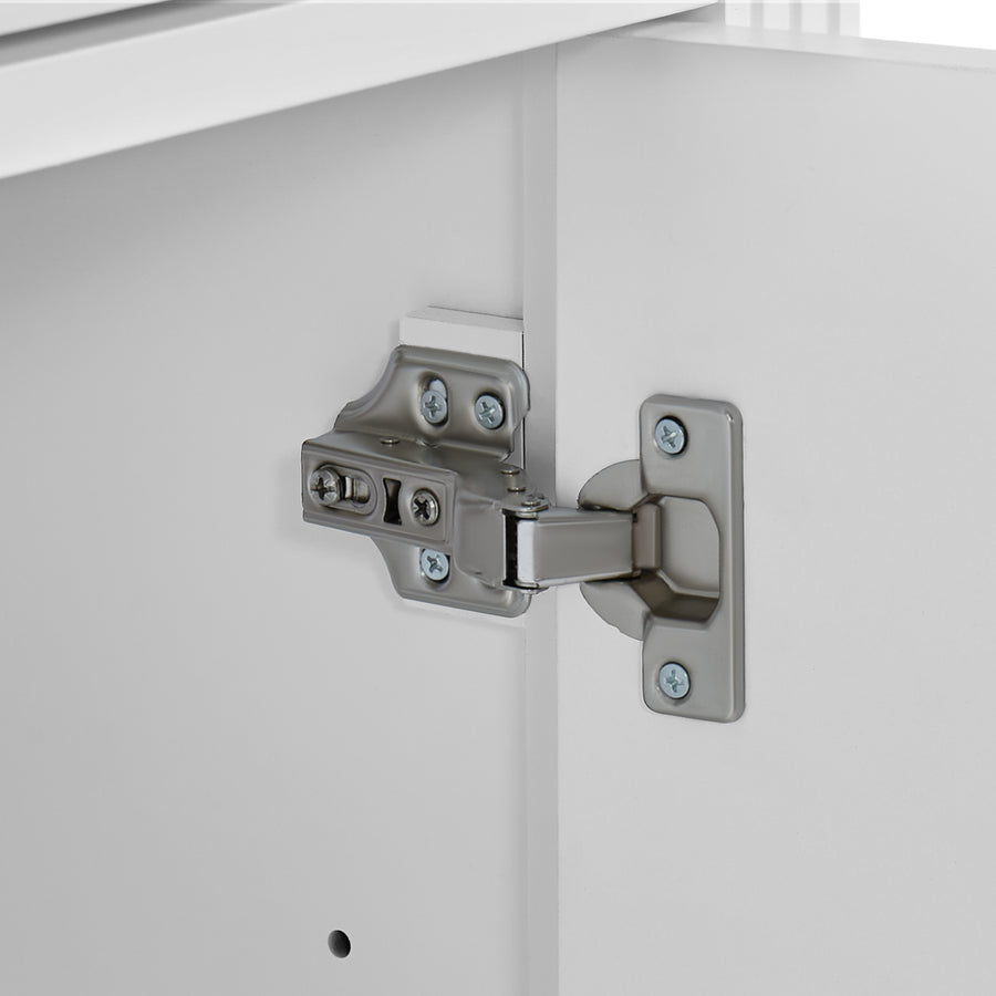 Close-up of a silver metal cabinet hinge mounted on a white cabinet door, with part of the cabinet frame visible.