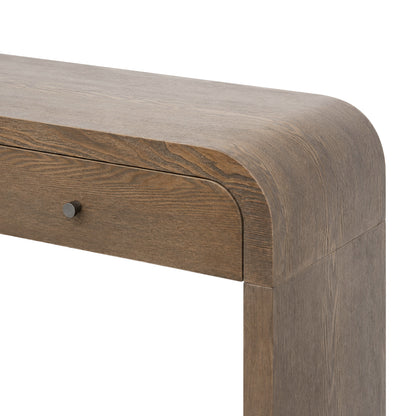 Close-up of a wooden table corner showing a medium brown wood grain finish, rounded apron, and a small round dark metal drawer knob on a white background.