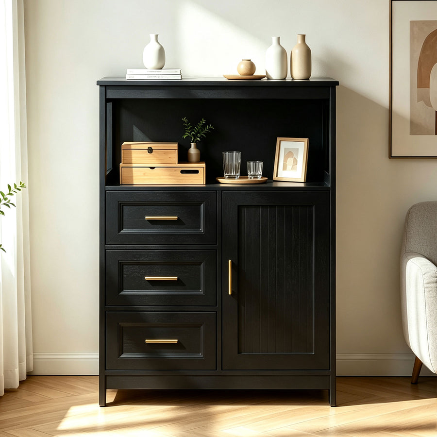 A tall black wooden cabinet with three drawers, a single door, and open shelving, styled in a bright living room with gold-tone handles and decorative objects on top and inside.