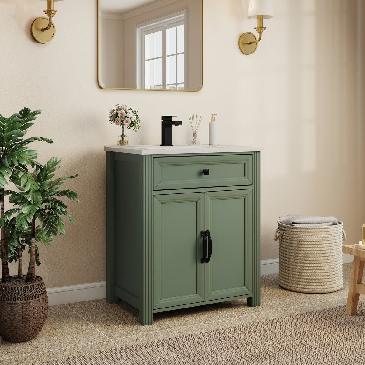 Olive green bathroom vanity cabinet with a countertop, black faucet, and black cabinet hardware, styled in a warm beige bathroom setting with a mirror, plant, and woven basket.
