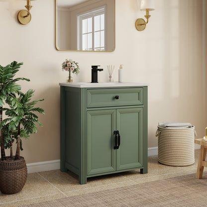 Olive green bathroom vanity cabinet with a countertop, black faucet, and black cabinet hardware, styled in a warm beige bathroom setting with a mirror, plant, and woven basket.
