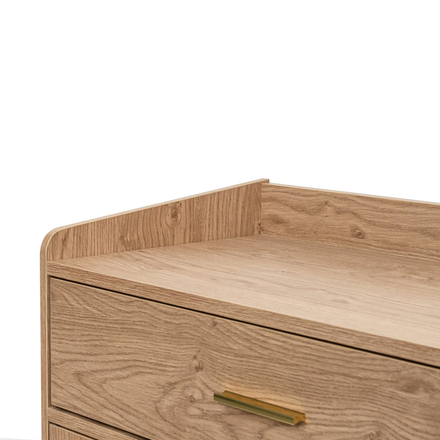 Close-up of a light natural  oak wood dresser or cabinet drawer with a curved front and a slim brass pull handle, set against a plain background.