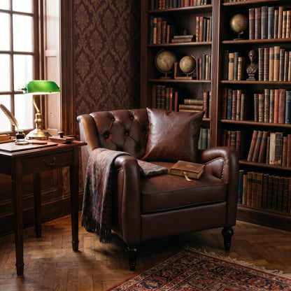 A classic Dark Brown solo leather Chesterfield armchair in a cozy, vintage-filled study with bookshelves, a green lamp, and a patterned throw blanket.