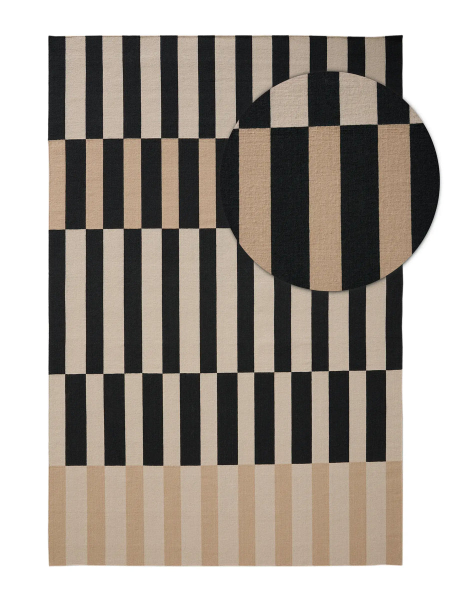 A rectangular area rug with a geometric pattern of black and beige vertical stripes and blocks, shown flat against a white background with a circular inset detail of the fabric texture. Hand made rugs