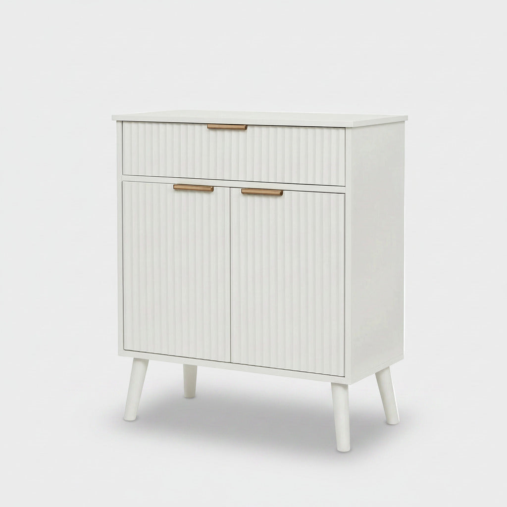 A mid-century modern white cabinet with ribbed doors and drawers, featuring slim gold metal handles and tapered legs, shown against a light gray background.