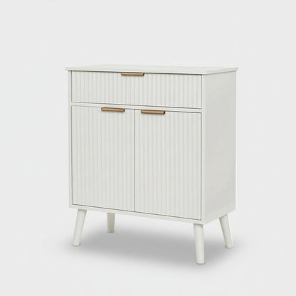 A mid-century modern white cabinet with ribbed doors and drawers, featuring slim gold metal handles and tapered legs, shown against a light gray background.