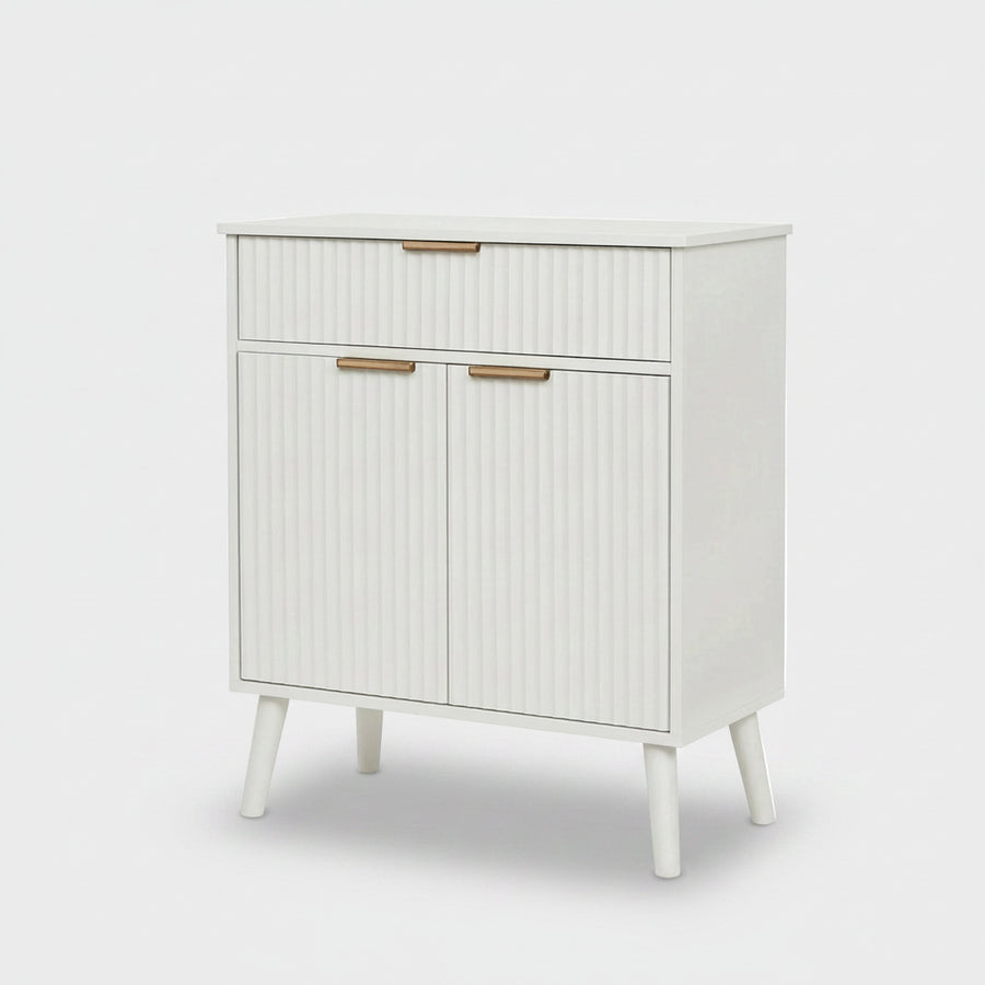 A mid-century modern white cabinet with ribbed doors and drawers, featuring slim gold metal handles and tapered legs, shown against a light gray background.