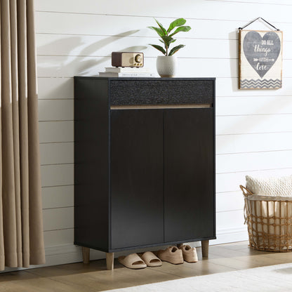 A tall black entryway cabinet with two doors and a textured top drawer section, styled in a bright room with a plant, books, a small radio, slippers, a curtain, and a basket nearby.