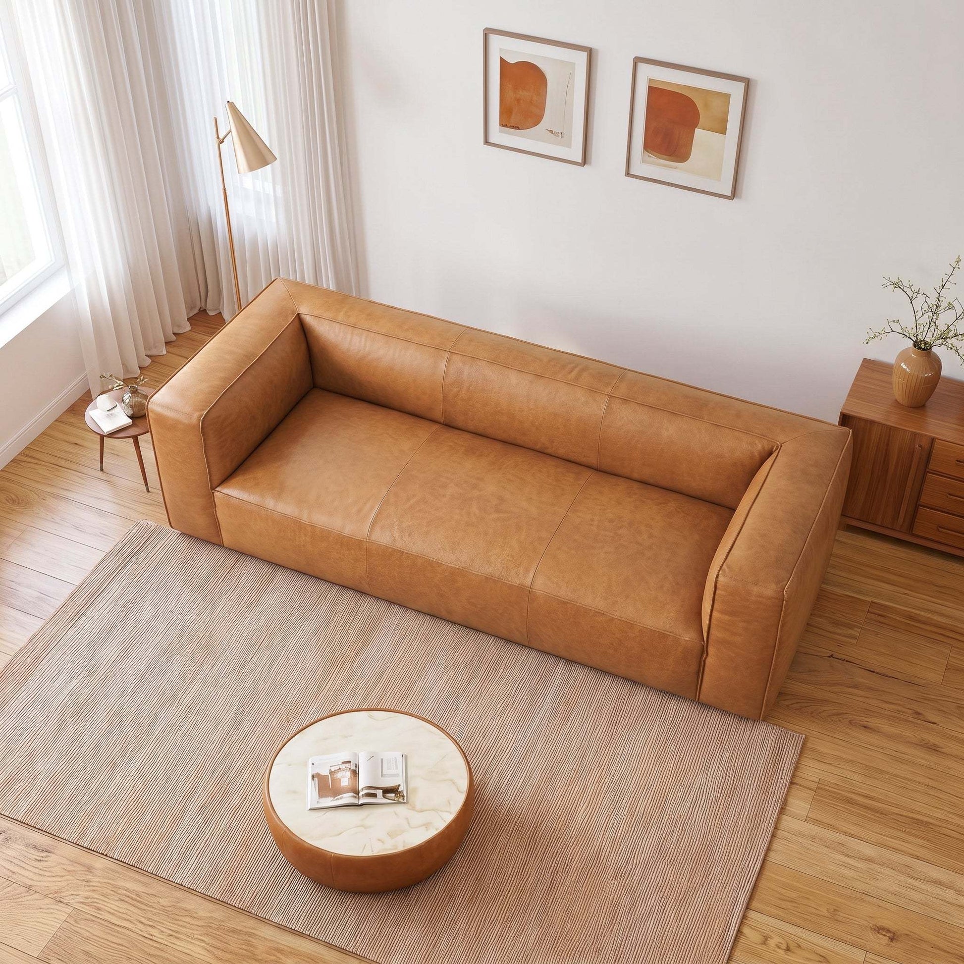 A modern tan leather sofa in a bright, minimalist living room with light wood floors, a beige rug, and neutral decor.