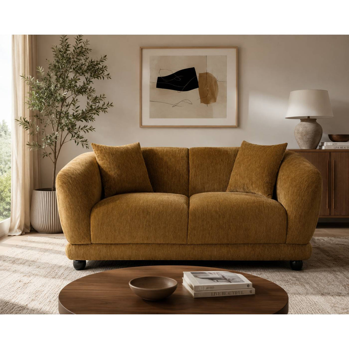 A mustard yellow textured fabric loveseat with two matching throw pillows, styled in a warm, modern living room setting with a wooden coffee table, potted plant, and abstract wall art.