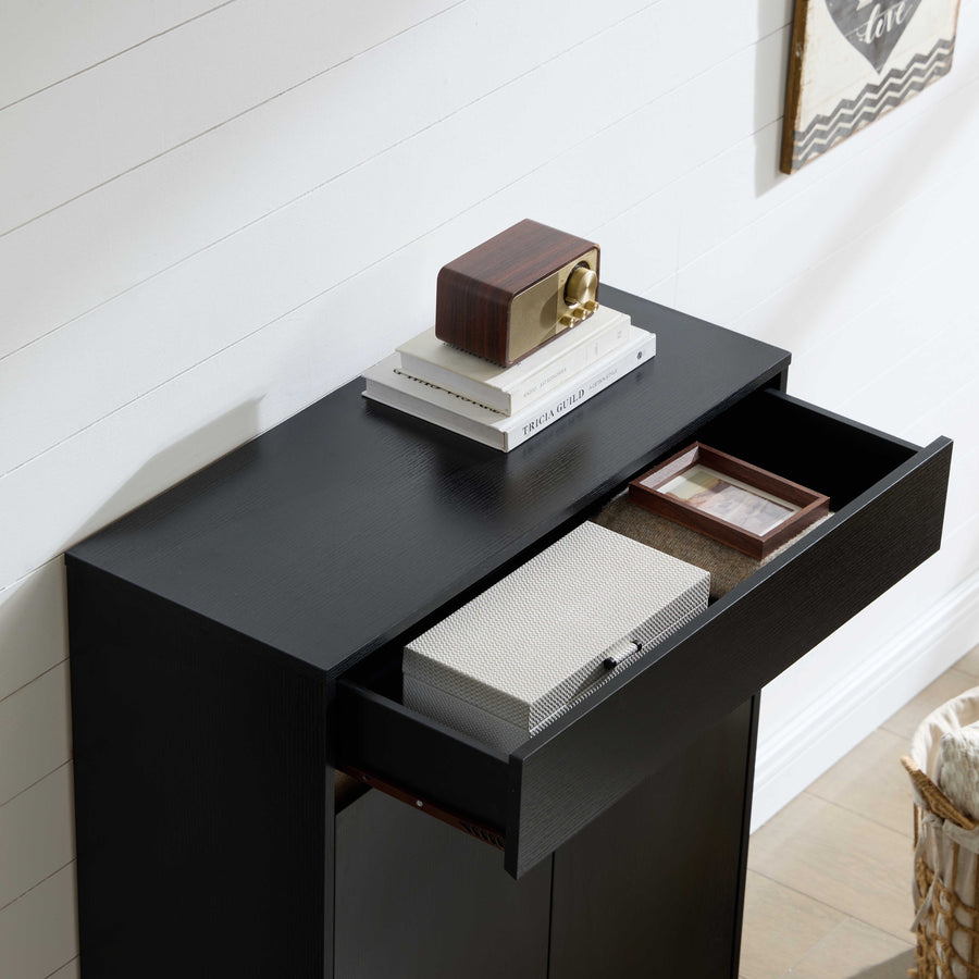 A black wooden console table with a lower cabinet and an open drawer, styled with books, a small radio, and a decorative box against a white shiplap wall.