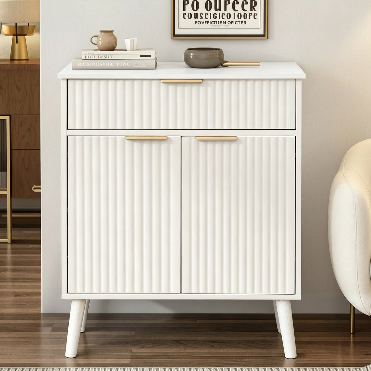 A modern white sideboard cabinet with vertical fluted panel doors and drawers, featuring slim gold metal handles and tapered white legs, styled in a contemporary living room setting.