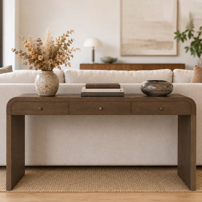 A dark brown wooden console table in a modern living room setting, styled with a vase of dried grass, books, and a decorative bowl on top.