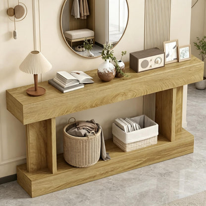 A light oak wood console table with a lower shelf, styled in a warm, modern interior. The table is decorated with a pleated table lamp, an open book, small vases with greenery, a vintage-style radio, and framed pictures.